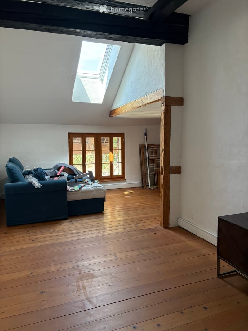 A spacious attic room with wooden floors, exposed wooden beams, and skylights. Features a sofa, bed, and a small table.