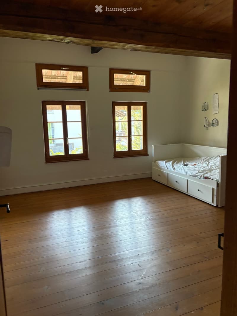 Spacious bedroom with wooden floors, four windows, and a built-in bed with drawers.