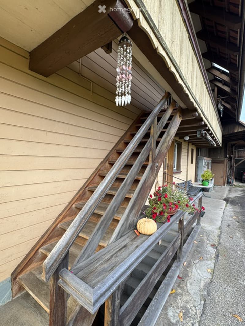 Wooden staircase leading up to a porch with a hanging decorative item, potted plants, and a small pumpkin on the railing.