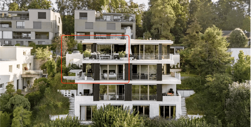 Modern multi-story residential building with large windows, balconies, and surrounding greenery.