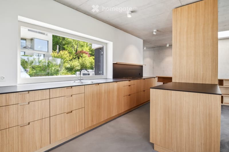 Modern kitchen with light wooden cabinets, a black countertop, and a large window offering a view of greenery outside.