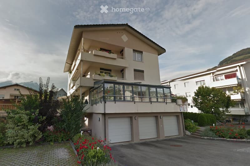 Multi-story residential building with beige facade, multiple balconies, and a garage area at the base.