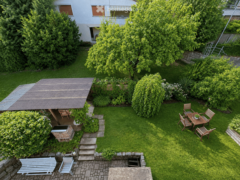 Well-maintained garden with a wooden table and chairs, a covered seating area, a bench, and a barbecue pit.