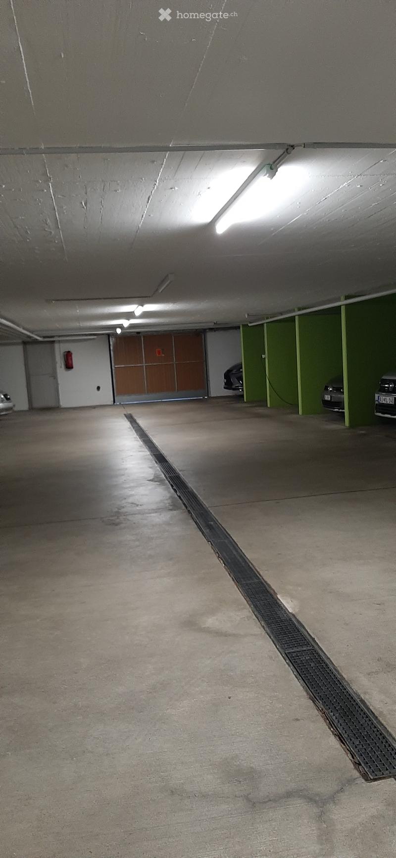 Underground parking area with concrete floors, green painted pillars, and a few parked cars visible in the background.