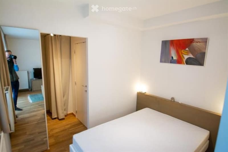 A modern bedroom with a wooden bed frame, a large mirror, a picture frame on the wall, and a curtained doorway leading to another room.
