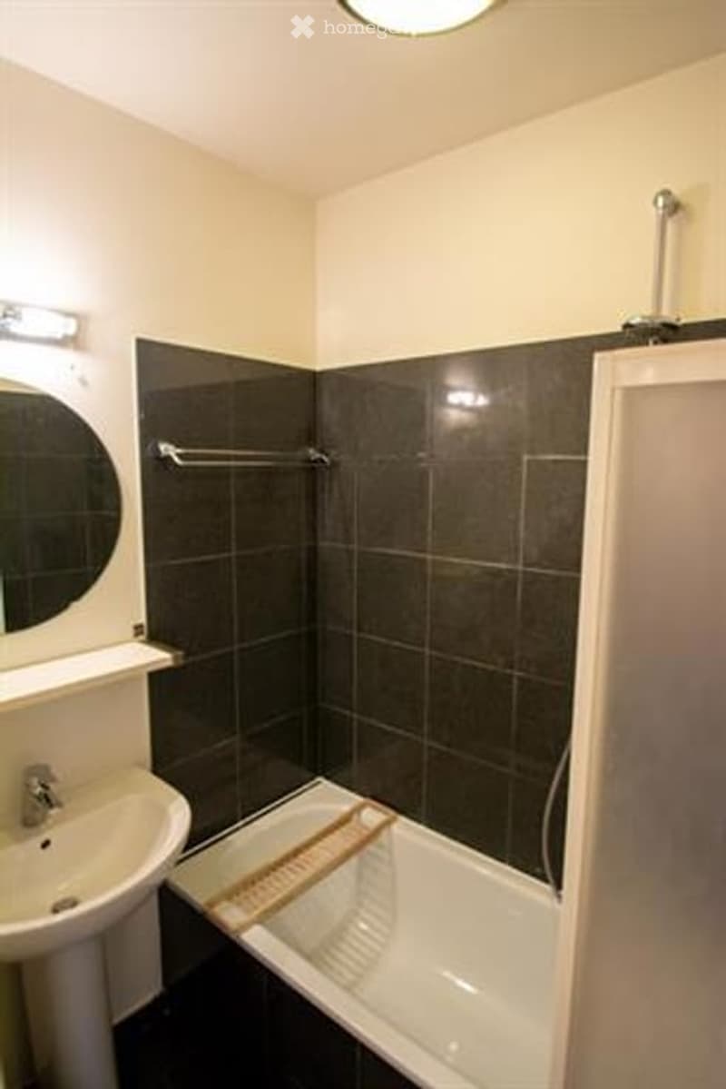 Modern bathroom with dark tiled walls, white bathtub, sink, and mirror. Features a towel rack and a shower curtain.