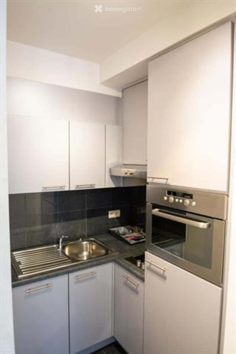 Modern kitchen with white cabinets, stainless steel sink, and built-in oven. Dark tiled backsplash and countertop.