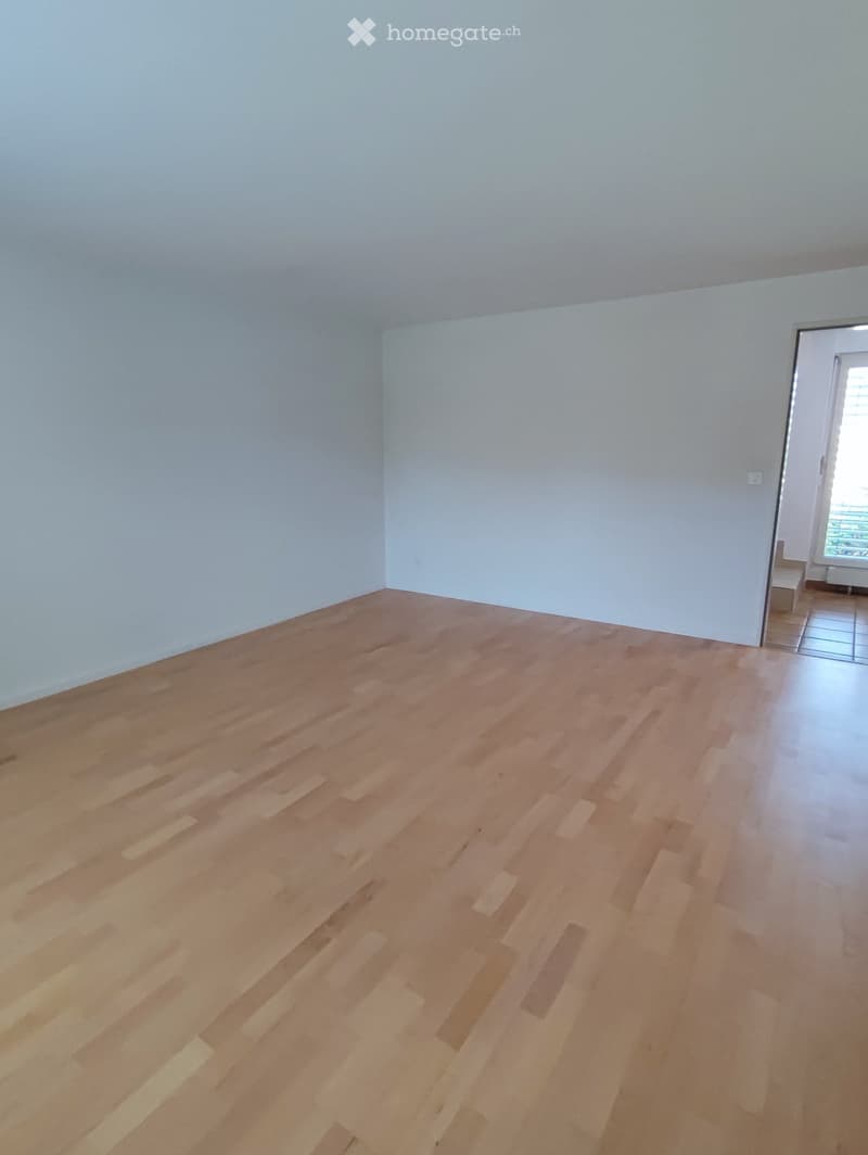 Empty room with light wooden flooring and white walls, featuring a doorway leading to another room.