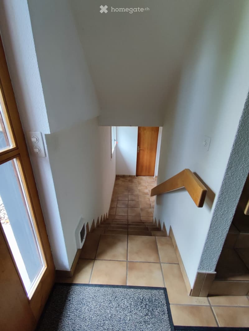 Hallway with tiled floor, wooden staircase, and a small rug at the bottom of the stairs.