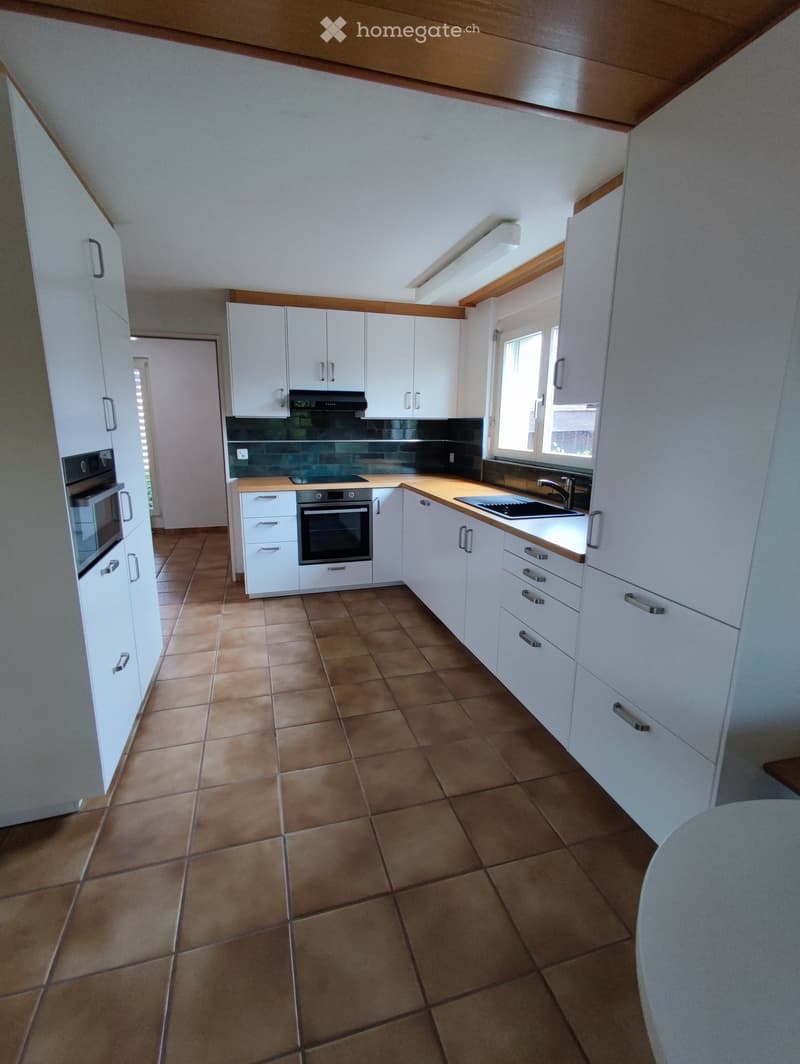 Modern kitchen with white cabinets, wooden countertops, tiled floor, and stainless steel appliances including an oven, microwave, and sink.