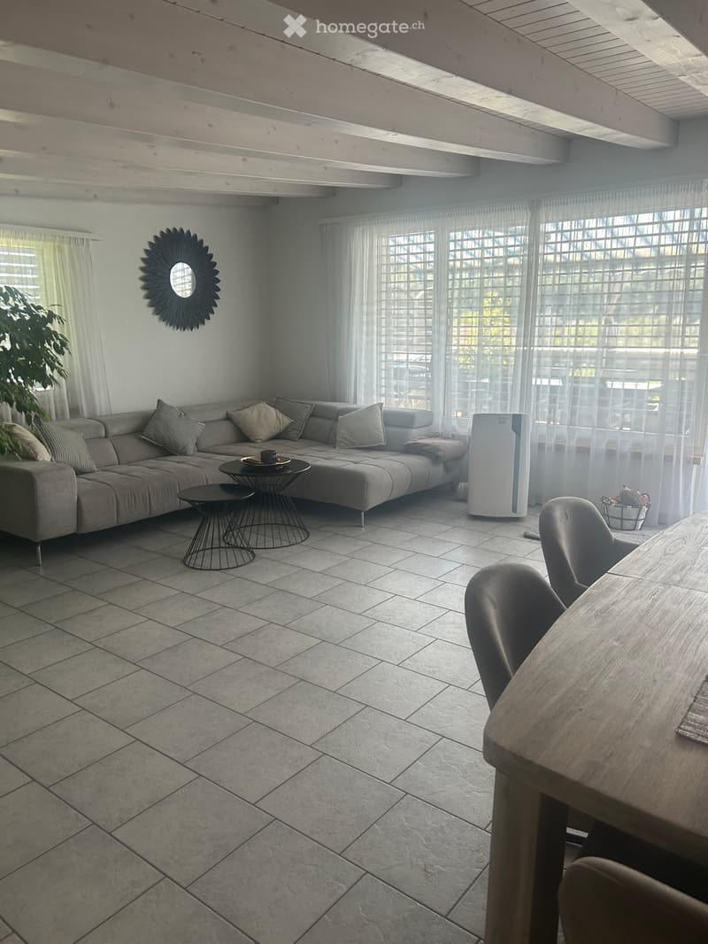 Living room with a grey sectional sofa, coffee table, dining table with chairs, air purifier, and a decorative mirror on the wall.