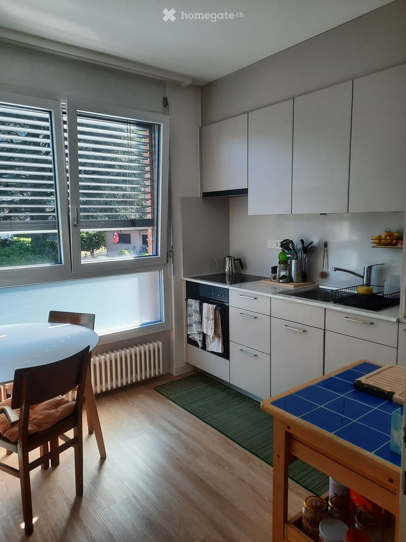 Modern kitchen with white cabinets, a round dining table, a wooden chair, and a small island with a blue tiled surface.