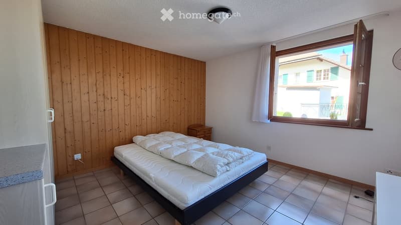 Bedroom with a double bed, nightstand, and large window with curtains. Wooden wall paneling on one side.