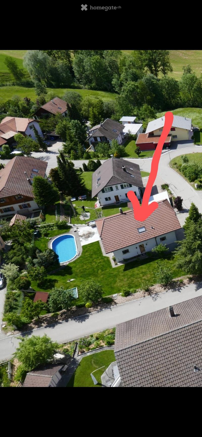 Aerial view of a residential neighborhood with multiple houses, a swimming pool, and surrounding greenery.