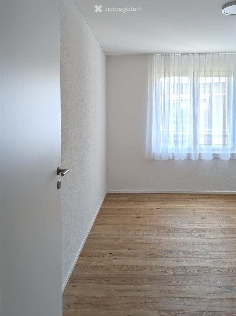 Empty room with wooden flooring, white walls, and a window with sheer curtains. No furniture or equipment is present.