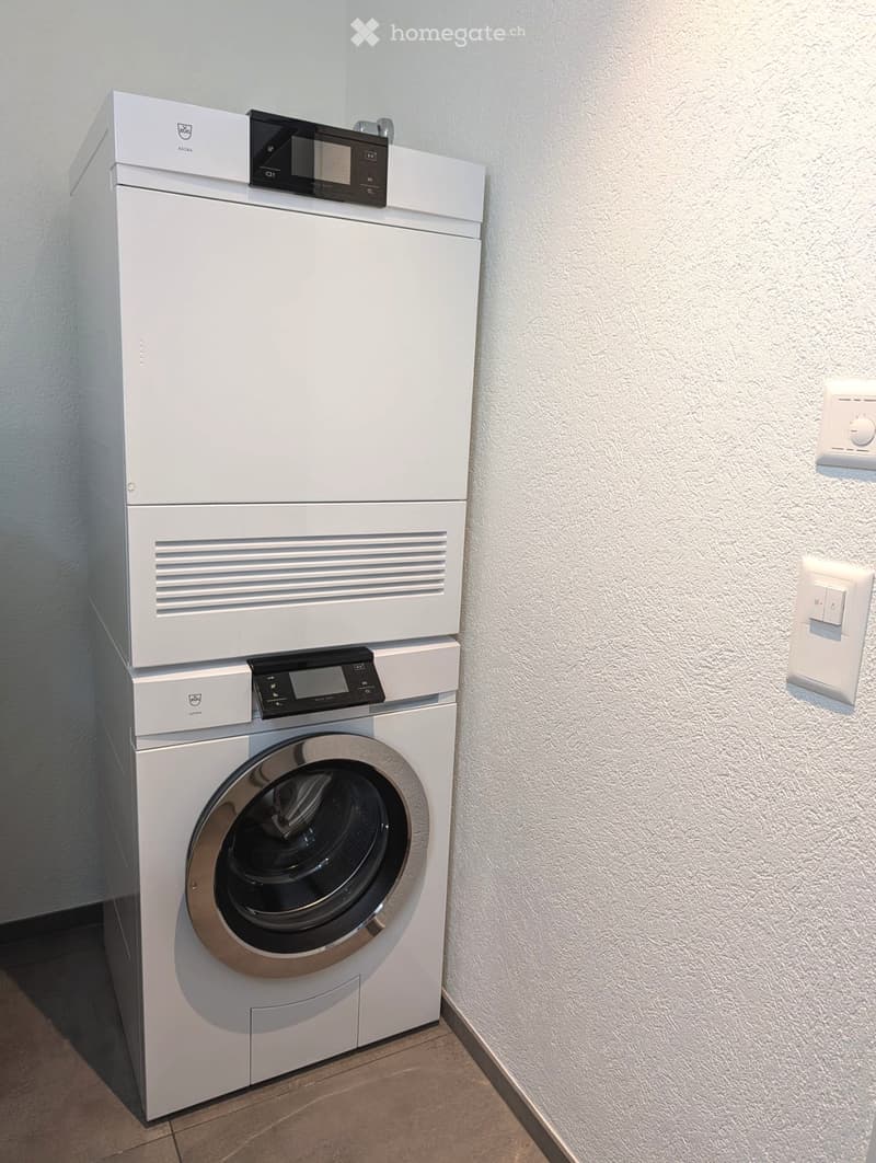 Modern bathroom with a white washing machine and dishwasher stacked vertically, featuring sleek digital control panels.
