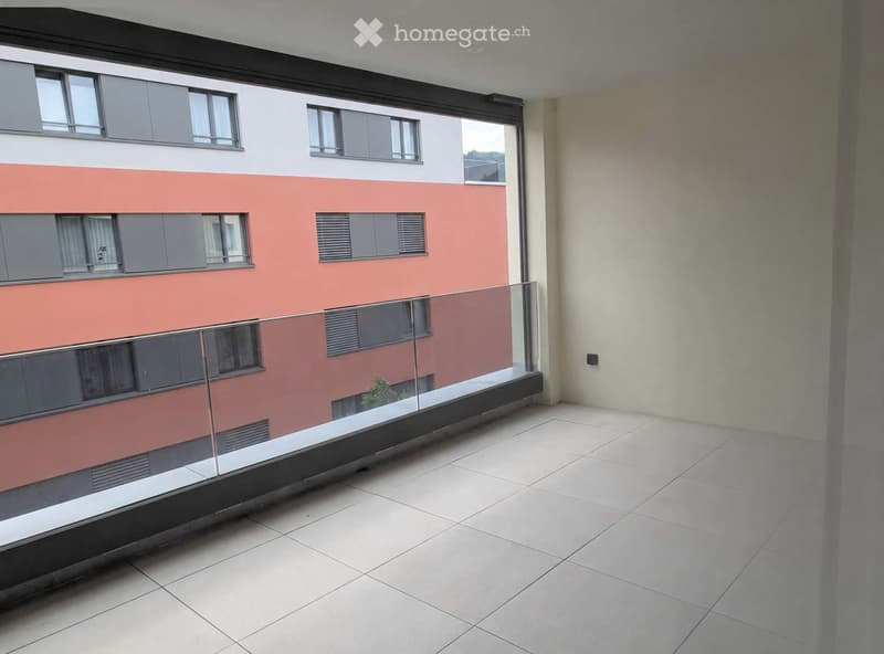 Balcony with tiled floor, glass railing, and view of a modern building with pink and white facade.