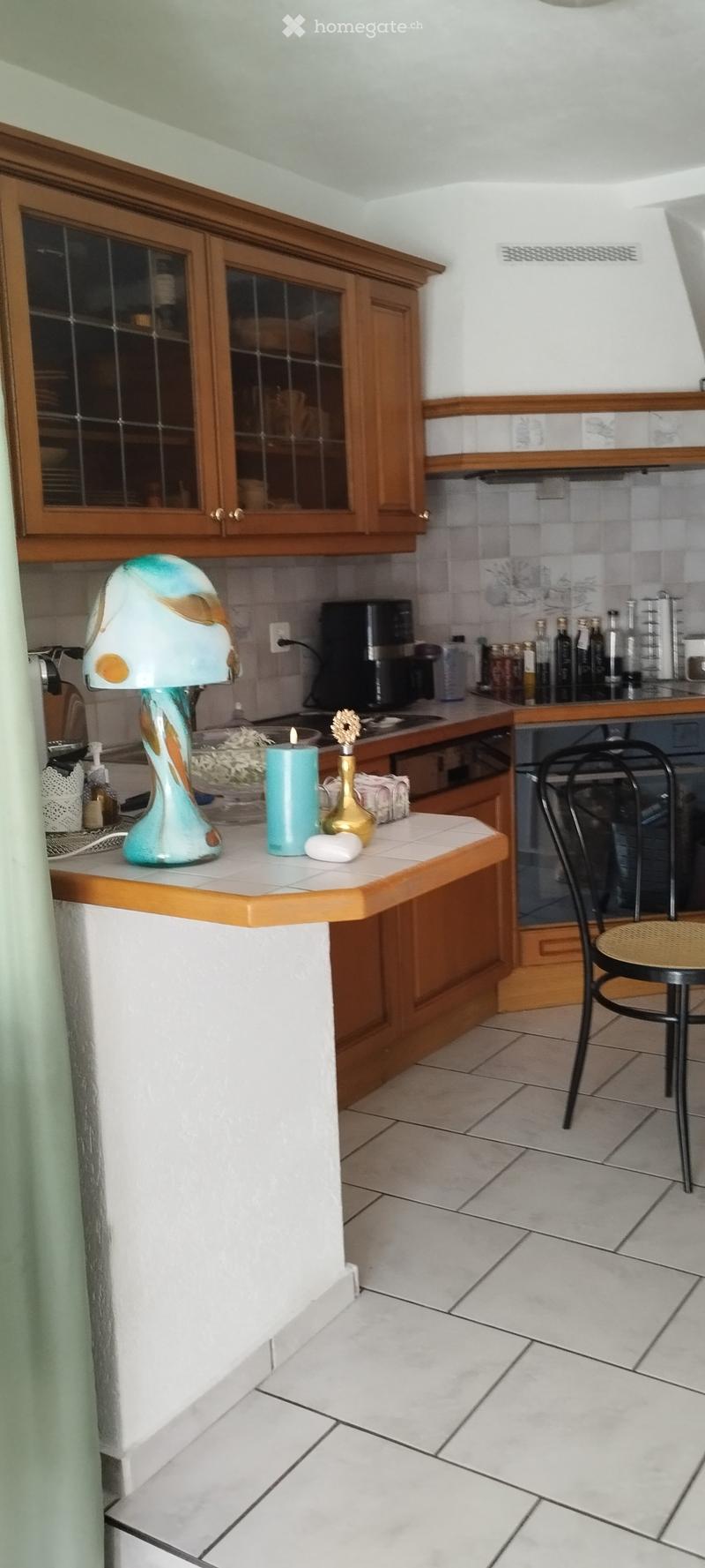 A modern kitchen with wooden cabinets, a countertop, a decorative lamp, and various small items including a candle and bottles.