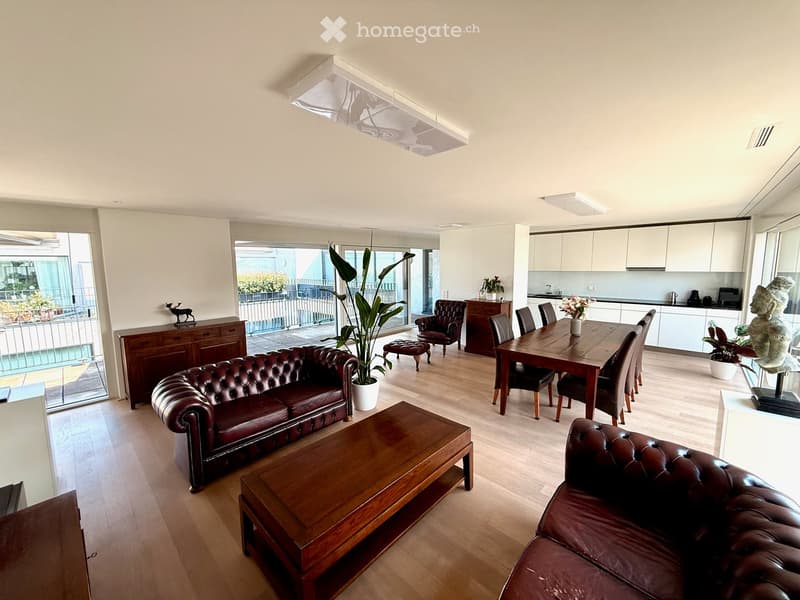 Open-plan living and dining area with wooden flooring, leather sofas, coffee table, dining table with chairs, and a balcony view.