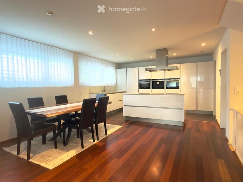 Modern kitchen and dining area with white cabinets, stainless steel appliances, wooden dining table, and chairs.
