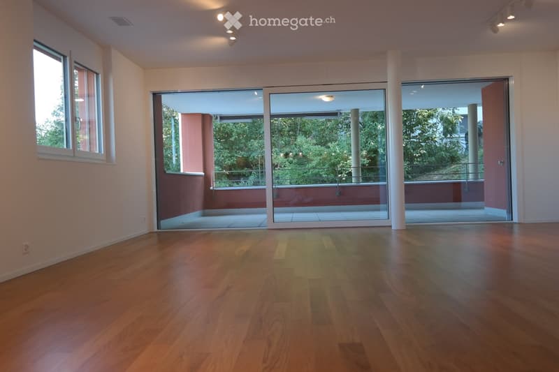 Empty room with wooden flooring, large windows, and sliding glass doors leading to a balcony area with outdoor views.