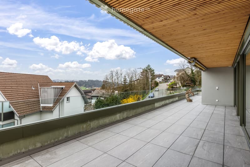 Modern balcony with tiled floor, wooden ceiling, glass railing, and scenic view of the neighborhood.
