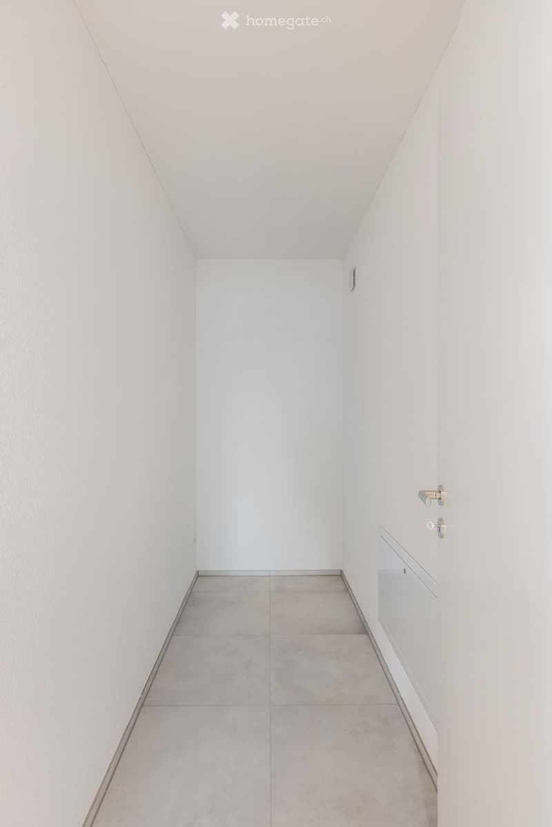 A clean, minimalist hallway with white walls, grey tiled floor, and a small built-in cabinet on the right side.