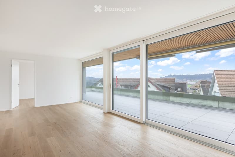 Bright, empty room with large sliding glass doors leading to a balcony, wooden flooring, and white walls.