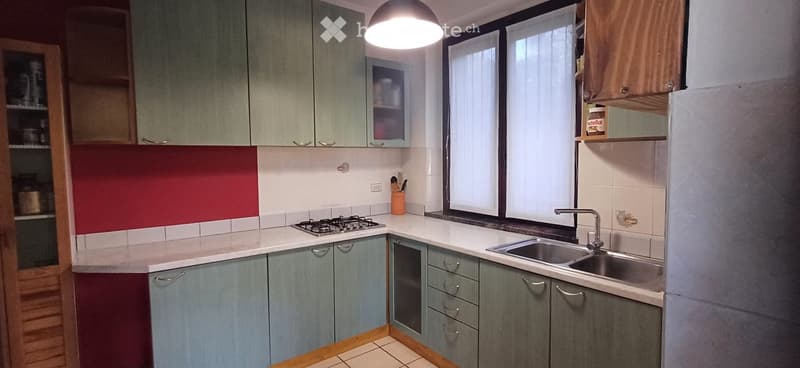 Modern kitchen with grey cabinets, white countertops, gas stove, sink, and a hanging light fixture.