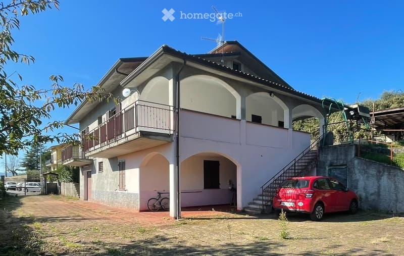 Two-story house with pink and white exterior, arched windows, balcony, and a red car parked in the driveway.