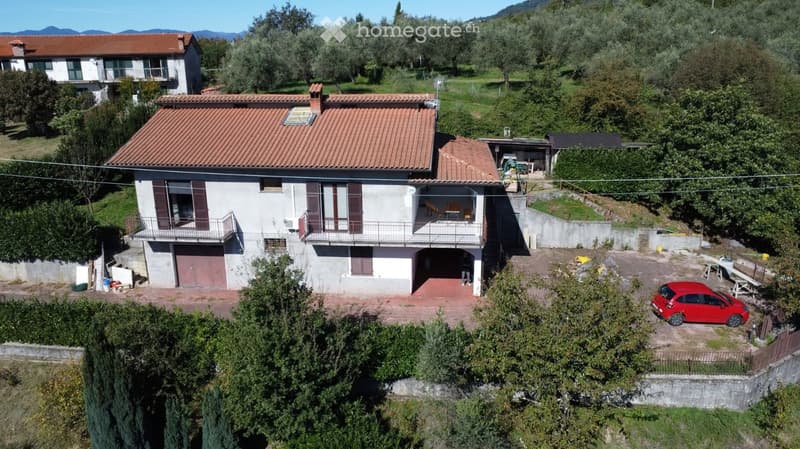 Two-story house with red-tiled roof, multiple windows, balconies, garage, and parking area.