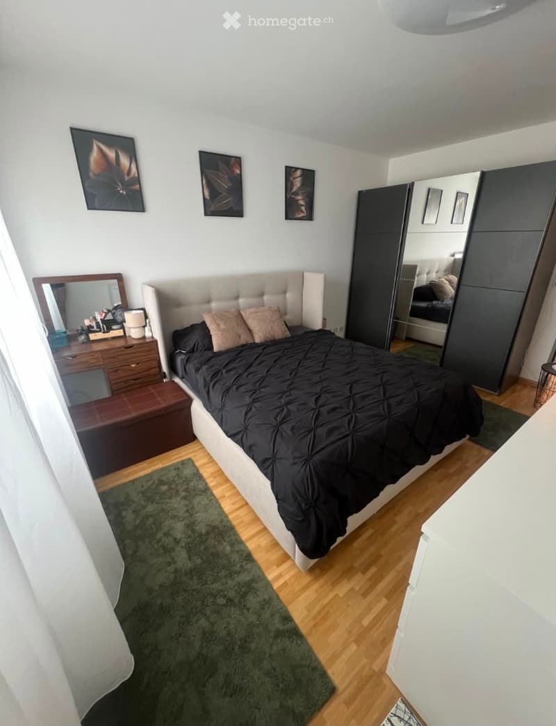Modern bedroom with a large bed, nightstand, mirror, wardrobe, and artwork on the walls.