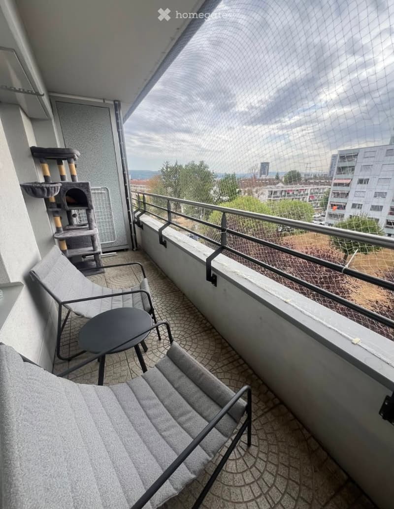 Balcony with a view, featuring a cat tree, two chairs, and a small table.