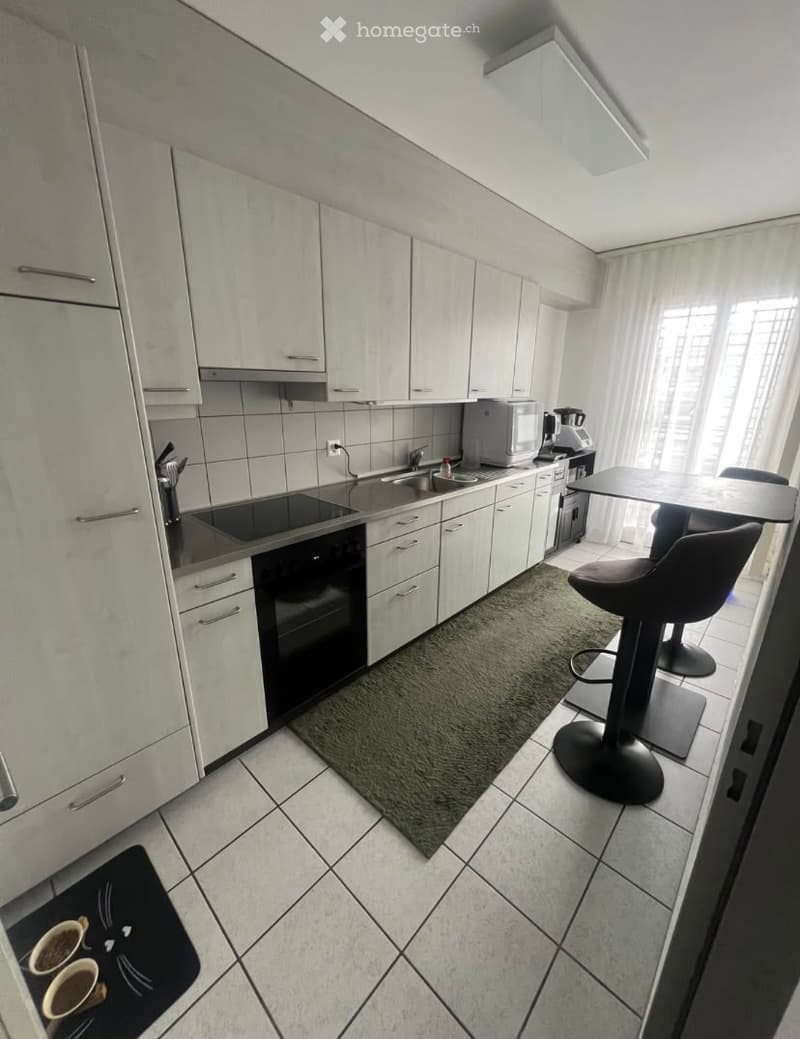 Modern kitchen with white cabinets, stainless steel appliances, and a small dining area with stools.