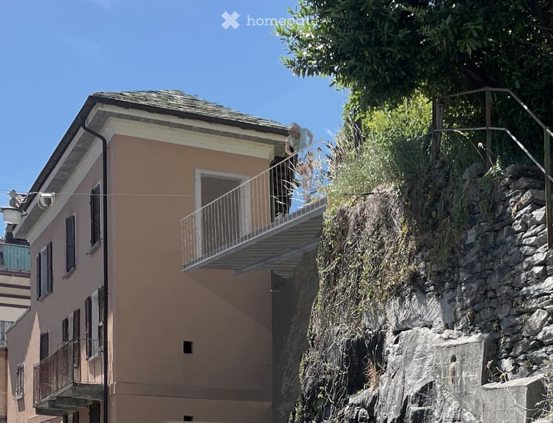 Two-story house with beige walls, multiple windows, and balconies overlooking a rocky hillside.