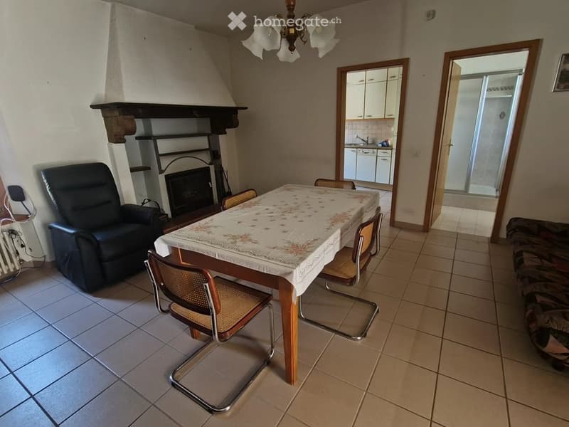 Living room with tiled floor, fireplace, sofa, dining table with chairs, and a view into the kitchen area.