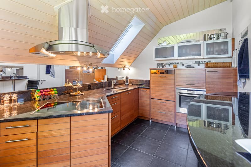 Modern kitchen with wooden cabinets, stainless steel appliances, island, sink, and microwave. Features a range hood and a bottle rack on the counter.