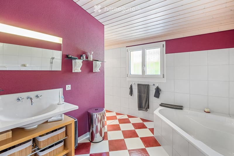 Modern bathroom with red accent wall, white tiles, and checkered floor. Features a sink, bathtub, mirror, towel rack, and storage shelf.