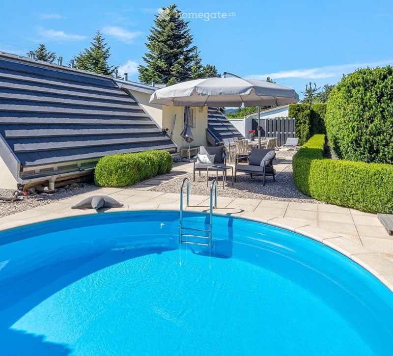 Outdoor area with a swimming pool, lounge chairs, umbrella, dining table, and surrounding greenery.
