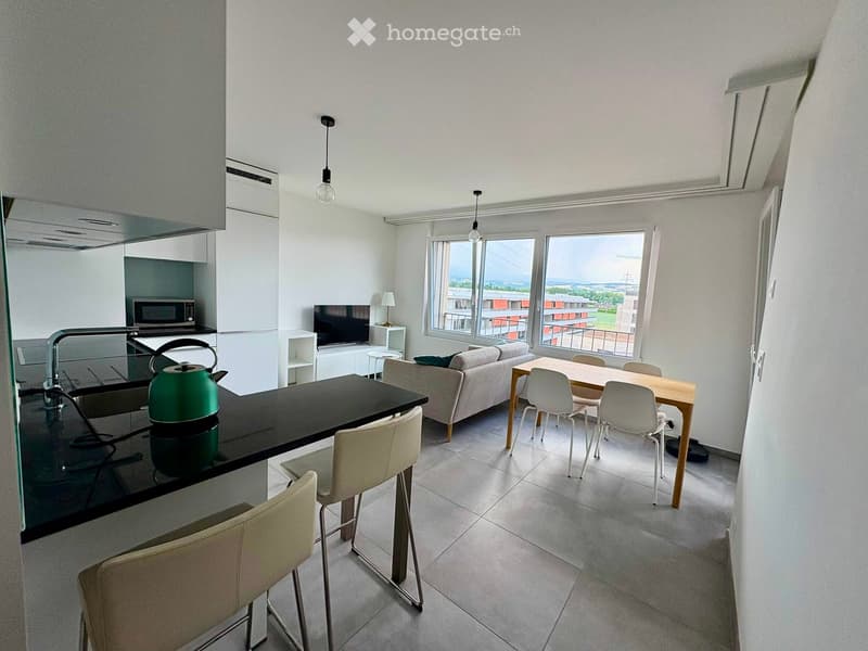Modern, open-concept living and dining area with large windows, a sofa, dining table, chairs, a kitchen counter with a teapot, and a microwave.