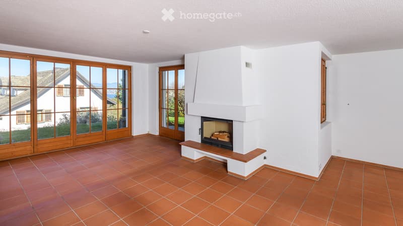 Bright living room with terracotta tiled floor, white walls, large wooden sliding doors, and a central fireplace with built-in seating.