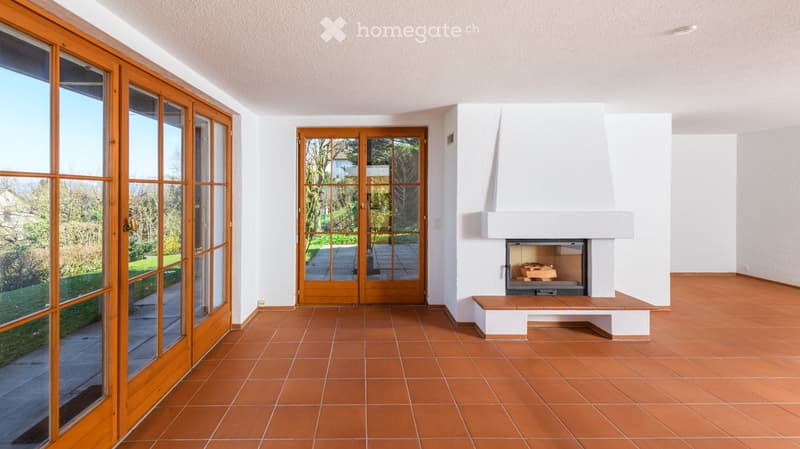Living room with terracotta tiled floor, white walls, large wooden sliding doors leading to a garden, and a built-in fireplace with a wooden bench.