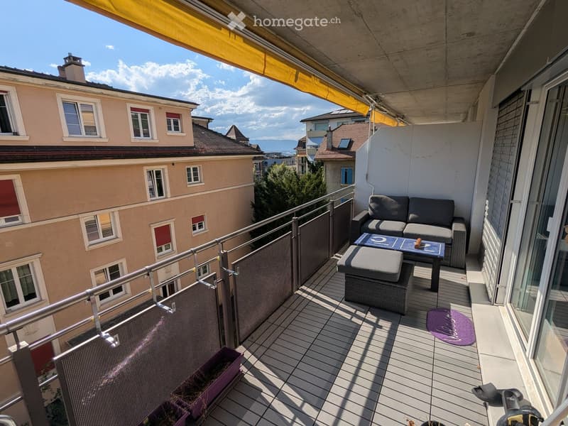 Balcony with wooden decking, metal railing, sofa, table, stool, rug, and bicycle.
