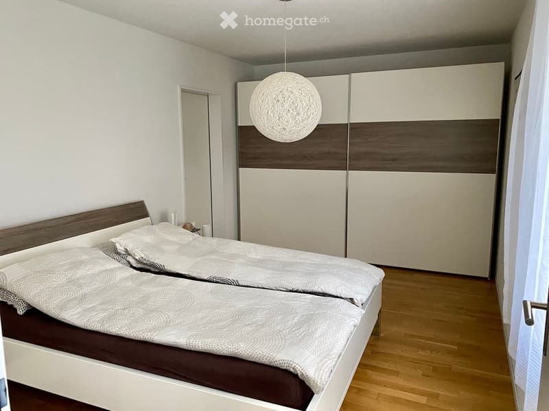 Modern bedroom with two single beds, white and grey bedding, a large wardrobe with wood and white panels, and a round pendant light hanging from the ceiling.