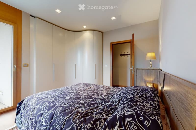 Modern bedroom with a large bed, sleek white wardrobe, nightstand with a lamp, and recessed ceiling lighting.