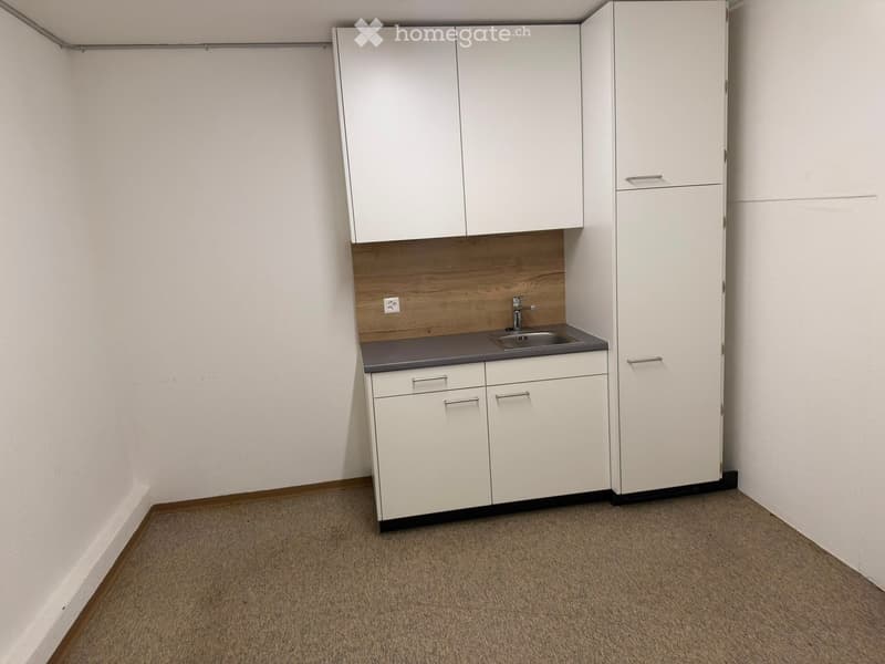Empty room with white cabinets, a sink, and a countertop, featuring a wooden backsplash and a gray countertop.