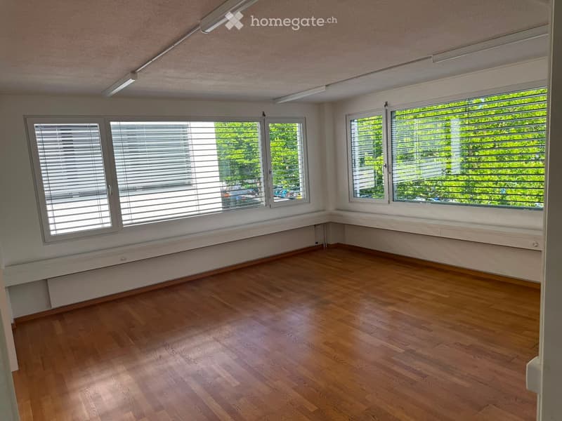 Empty room with wooden flooring, large windows with blinds, and white walls.