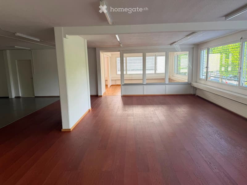 Empty room with wooden flooring, large windows with blinds, and white walls. No furniture or equipment present.