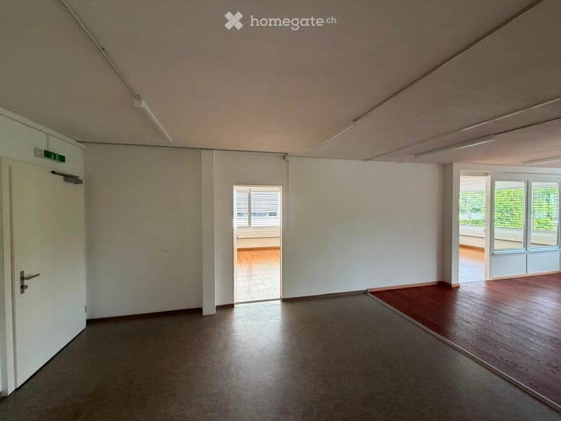 Empty room with white walls, wooden flooring, and large windows. No furniture or equipment present.