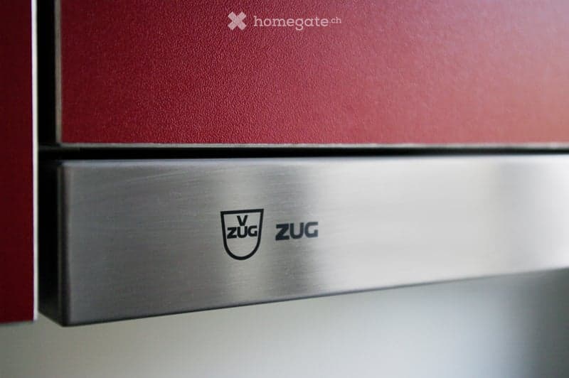 Close-up of a stainless steel dishwasher with the brand name "ZUG" visible on the handle.
